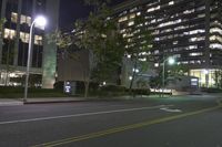 a night scene shows empty road in the distance in front of modern tall buildings in an urban city