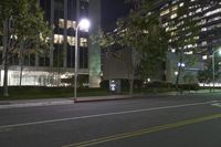 a night scene shows empty road in the distance in front of modern tall buildings in an urban city