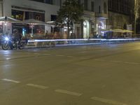 motorcyclists and pedestrians are sitting outside the sidewalk cafe at night on a city street