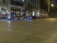 motorcyclists and pedestrians are sitting outside the sidewalk cafe at night on a city street