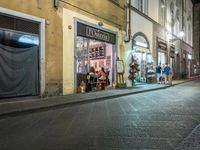 a street corner with people eating at tables and parked cars in front of it at night