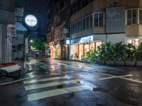 a wet street with a motorcycle parked in front of a large shop at night near street lamps