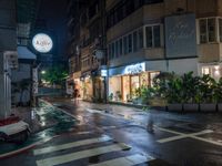 a wet street with a motorcycle parked in front of a large shop at night near street lamps