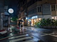 a wet street with a motorcycle parked in front of a large shop at night near street lamps