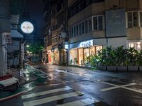 a wet street with a motorcycle parked in front of a large shop at night near street lamps