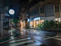 a wet street with a motorcycle parked in front of a large shop at night near street lamps