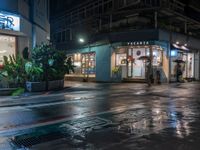 a wet street with a motorcycle parked in front of a large shop at night near street lamps