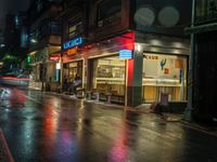 a wet street with a motorcycle parked in front of a large shop at night near street lamps