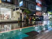 a wet street with a motorcycle parked in front of a large shop at night near street lamps