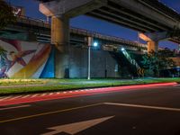 a painting is hanging up next to the highway on the side of a bridge at night