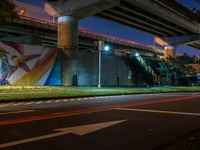 a painting is hanging up next to the highway on the side of a bridge at night