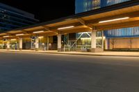 a long street lined with tall buildings at night with a bus stop on the right side