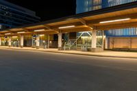 a long street lined with tall buildings at night with a bus stop on the right side