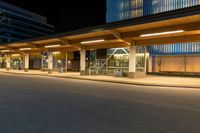 a long street lined with tall buildings at night with a bus stop on the right side