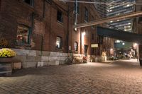 a sidewalk with a building and many flowers on it at night, with the lights turned on