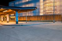 the night scene shows the entrance to an office building and a tall glass fronted building