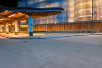 the night scene shows the entrance to an office building and a tall glass fronted building