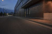 a person is on a skateboard by a building at night in the street by a curb with a yellow light and street lamp