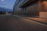 a person is on a skateboard by a building at night in the street by a curb with a yellow light and street lamp