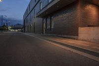 a person is on a skateboard by a building at night in the street by a curb with a yellow light and street lamp