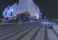 the view of a modern building lit by blue lights at night with benches to be seen