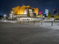 a night shot of the modern building with lights on it's side and city skyline in the distance