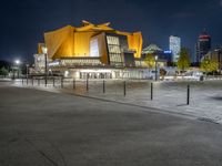 a night shot of the modern building with lights on it's side and city skyline in the distance