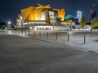 a night shot of the modern building with lights on it's side and city skyline in the distance