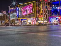 a night shot of an intersection with many neon lights and buildings in the background and one street sign is lit up