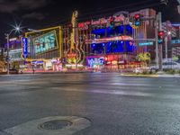 a night shot of an intersection with many neon lights and buildings in the background and one street sign is lit up