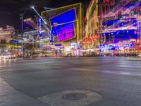 a night shot of an intersection with many neon lights and buildings in the background and one street sign is lit up