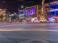 a night shot of an intersection with many neon lights and buildings in the background and one street sign is lit up