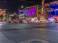 a night shot of an intersection with many neon lights and buildings in the background and one street sign is lit up