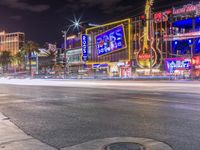 a night shot of an intersection with many neon lights and buildings in the background and one street sign is lit up