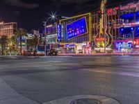 a night shot of an intersection with many neon lights and buildings in the background and one street sign is lit up
