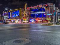 a night shot of an intersection with many neon lights and buildings in the background and one street sign is lit up