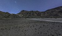 a night shot with rocks, dirt, and stars lit up the sky above some mountains