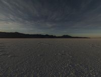 a big wide open desert with tracks of people riding horses in the background at sunset