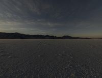 a big wide open desert with tracks of people riding horses in the background at sunset