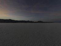 a big wide open desert with tracks of people riding horses in the background at sunset