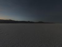 a big wide open desert with tracks of people riding horses in the background at sunset