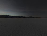 a big wide open desert with tracks of people riding horses in the background at sunset