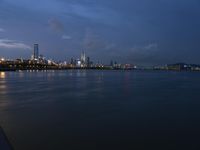 large water area with city lights and skyline in background at dusk time and blue sky