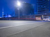 an empty street with buildings in the background at night and a road crossing above it