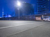 an empty street with buildings in the background at night and a road crossing above it