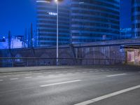 an empty street with buildings in the background at night and a road crossing above it
