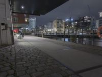 the pier of the city with ships is lit up at night with people sitting and walking