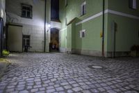 a street at night with green walls and cobblestone floorings with a stone path to a doorway