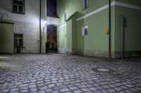 a street at night with green walls and cobblestone floorings with a stone path to a doorway