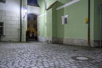 a street at night with green walls and cobblestone floorings with a stone path to a doorway